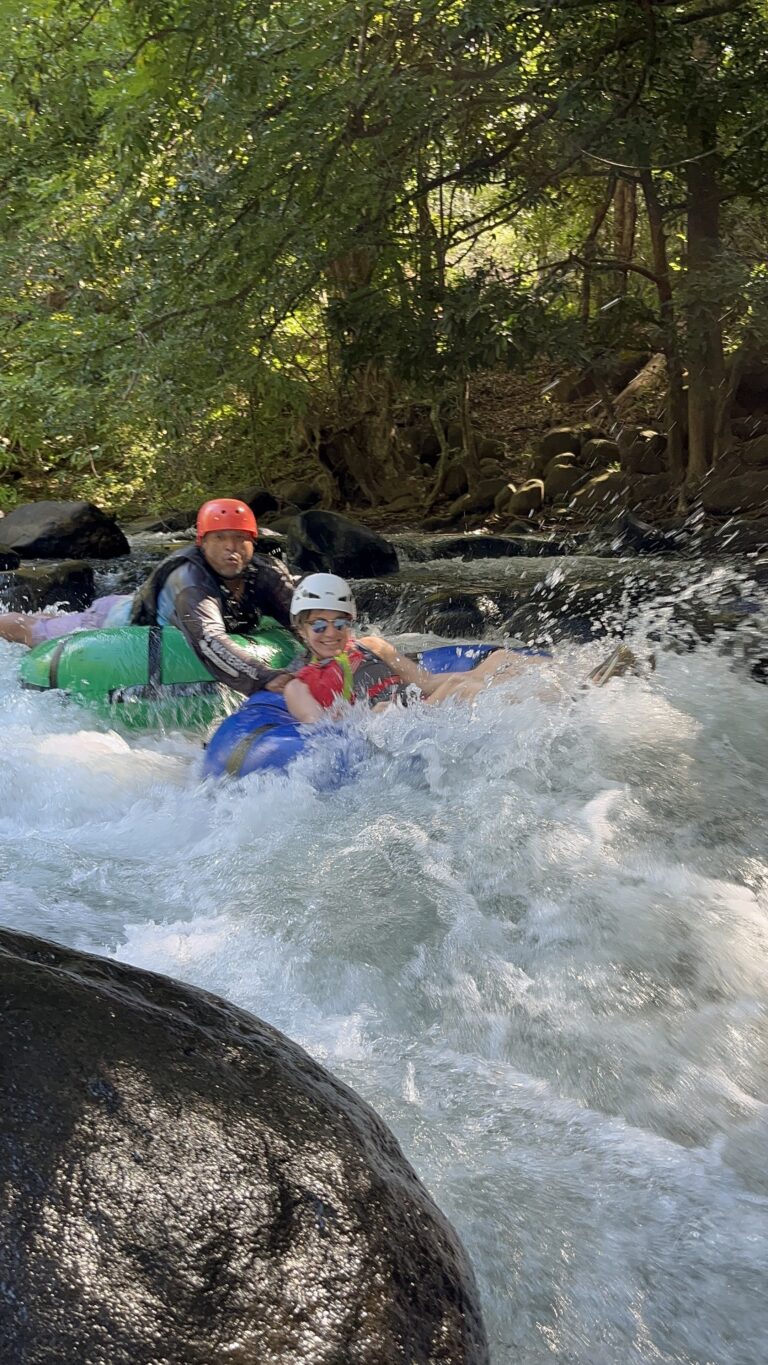 Smiling guest in helmet and life vest tubing down river rapids
